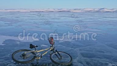人和他的自行车在冰上。 骑自行车的人穿着灰色的羽绒服，背包和头盔。 冰冻湖的冰